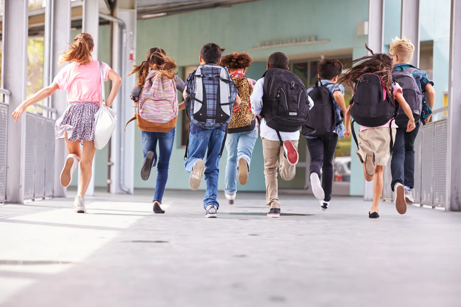 A group of school children running toward the school entrance with backpacks